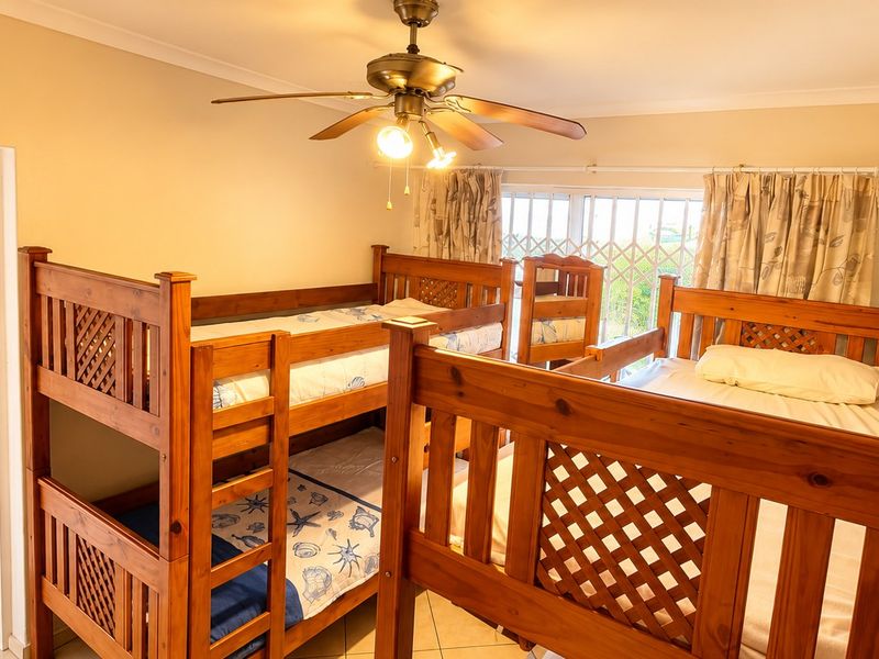 A bedroom featuring tiled flooring, a ceiling fan, and a security gate over the window, currently configured with multiple wooden bunk beds.