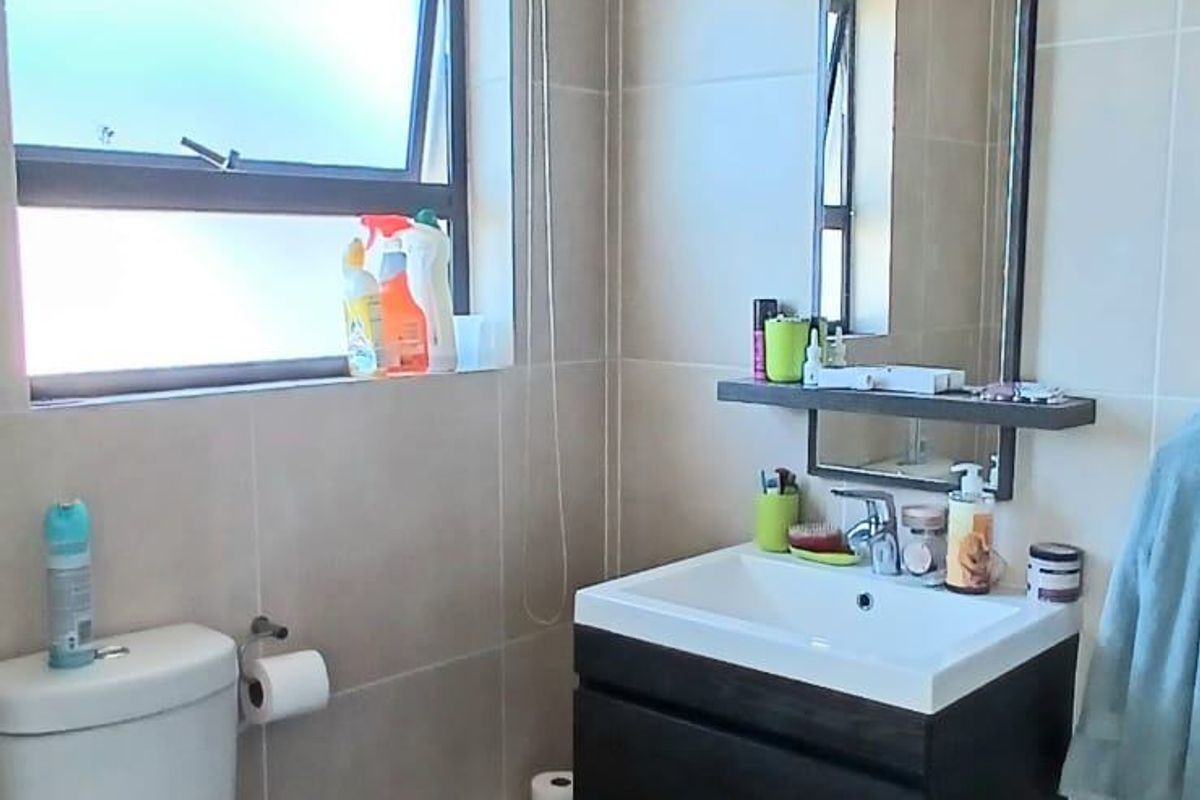A functional bathroom featuring a wall-mounted vanity with a basin, a toilet, and neutral floor-to-ceiling wall tiles.