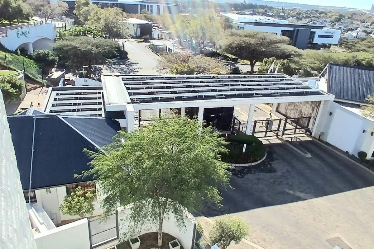 Aerial view of the apartment complex entrance featuring a security gate and solar panel installation on the roof structure.