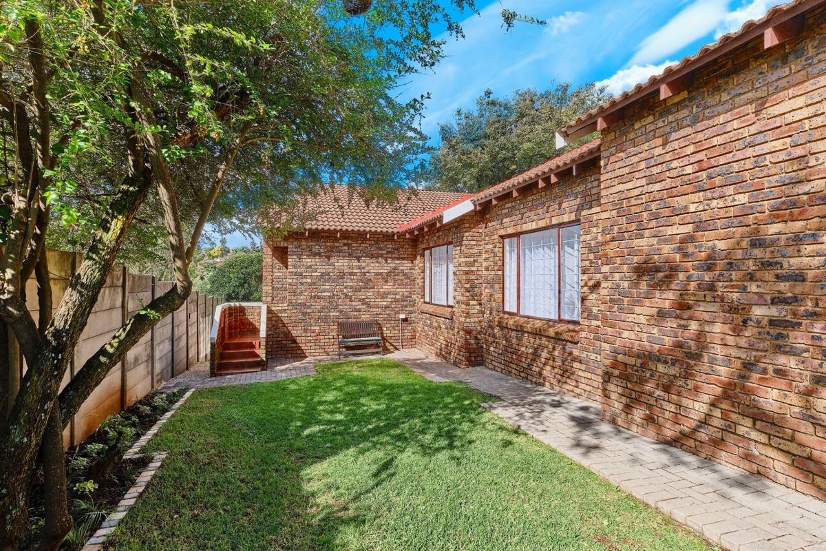 A private rear garden featuring a well-maintained lawn, paved pathways, and a classic face brick townhouse exterior with secure window fittings.