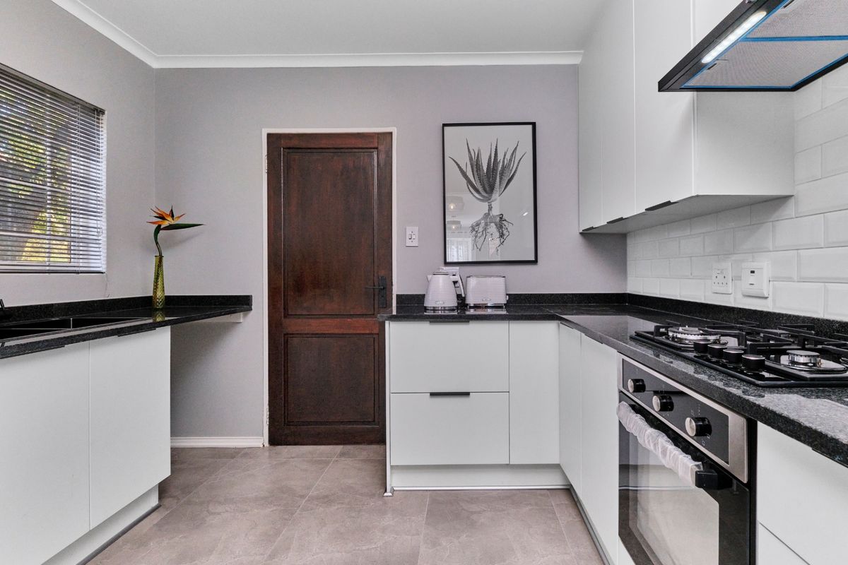 Modern kitchen featuring white cabinetry, dark granite countertops, subway tile backsplash, and integrated gas hob with oven.