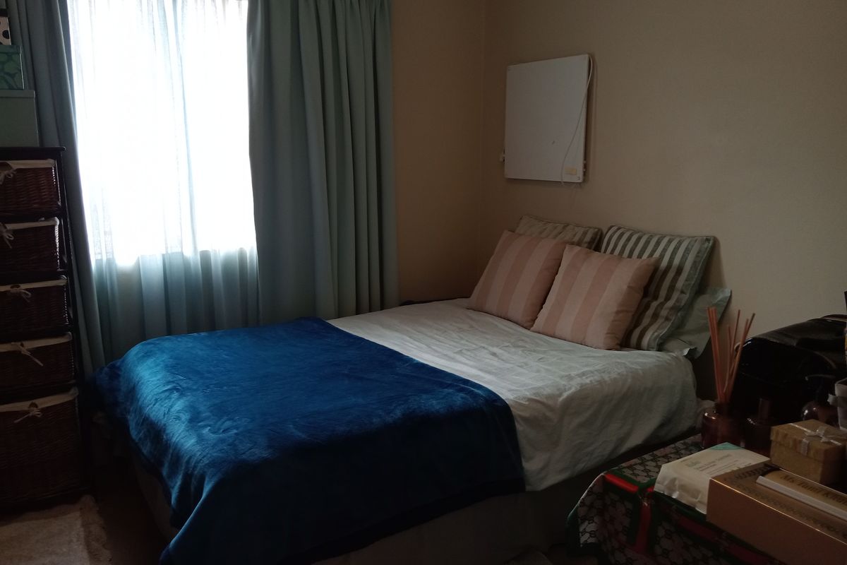 A standard bedroom featuring a wall-mounted electric heater and natural light from the window.