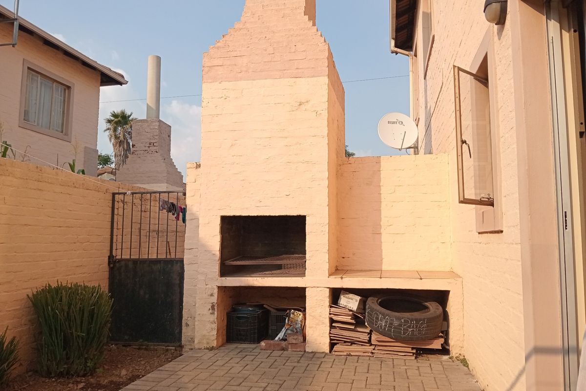 Rear courtyard area featuring a built-in brick braai, paved patio flooring, and secure boundary walling.