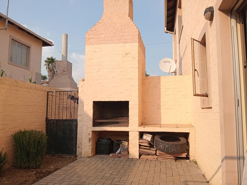 Rear courtyard area featuring a built-in brick braai, paved patio flooring, and secure boundary walling.