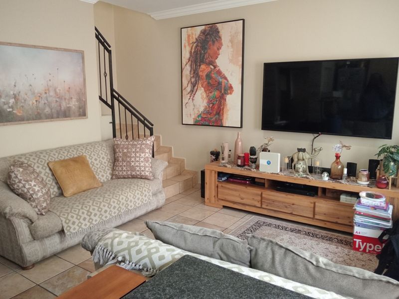A comfortable living room featuring tiled flooring, a wrought iron staircase railing, and neutral wall tones, providing a functional and inviting space.