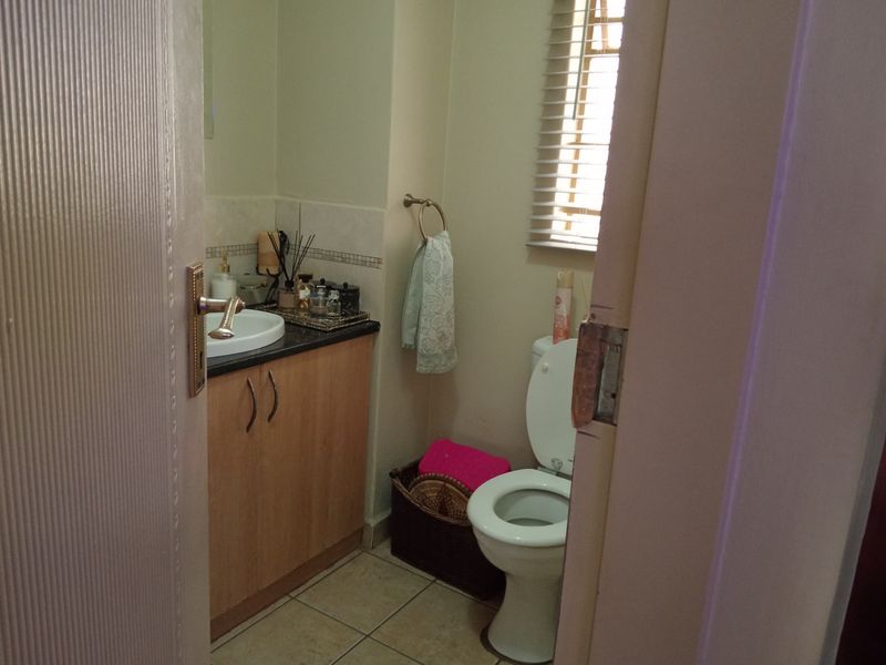 A compact guest bathroom featuring a vanity cabinet with granite countertop, drop-in basin, and standard toilet, finished with tiled flooring and venetian blinds.