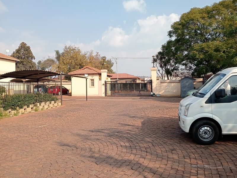 Front exterior view of the townhouse complex featuring a paved driveway, secure gated entrance, and covered carport parking area.