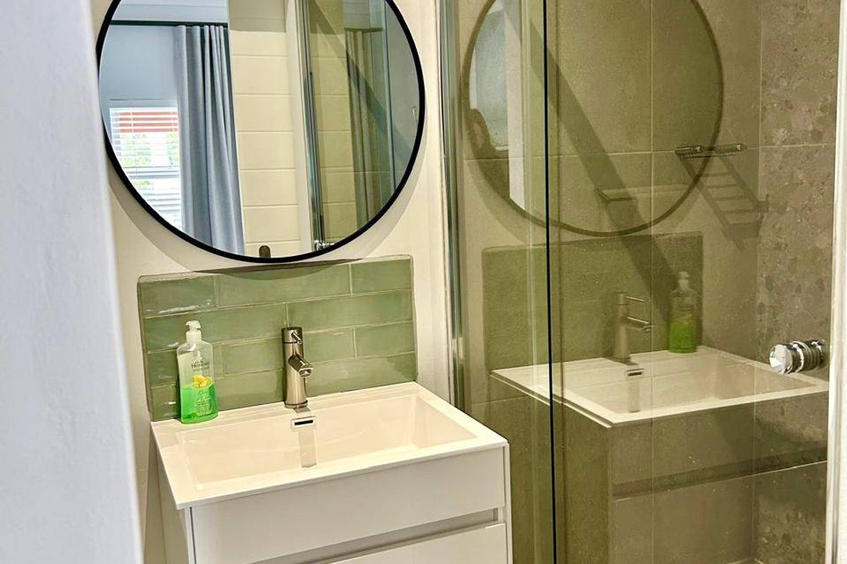 Modern bathroom featuring a wall-mounted vanity with basin, stylish green subway tile backsplash, and a spacious walk-in shower with glass enclosure.