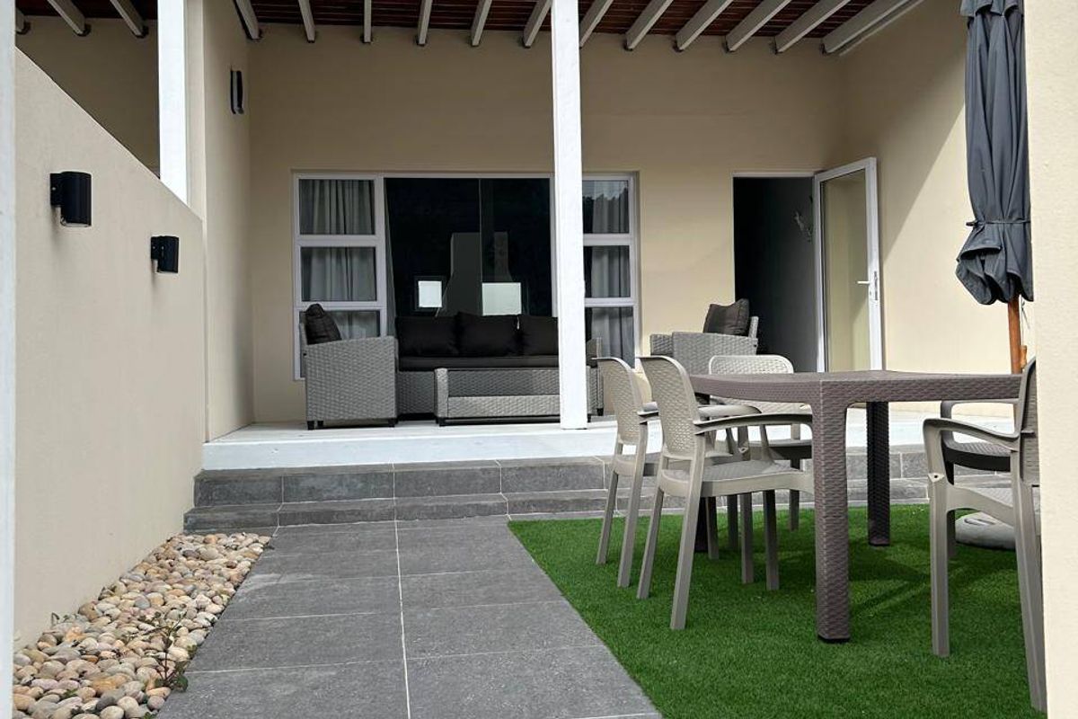 A well-maintained covered patio area featuring tiled flooring, artificial grass, and a balustrade, providing a functional outdoor living space.