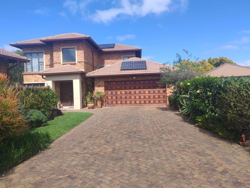 A well-maintained double-story face brick cluster home featuring a paved driveway, double garage, and installed solar panels.