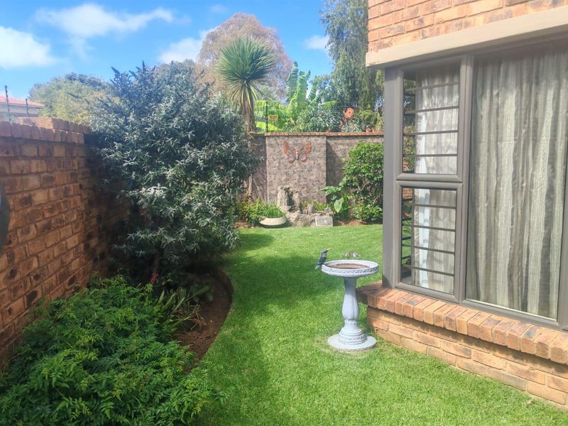 A private rear garden featuring a well-maintained lawn, established greenery, and face brick boundary walls, adjacent to the main dwelling with aluminium window frames.