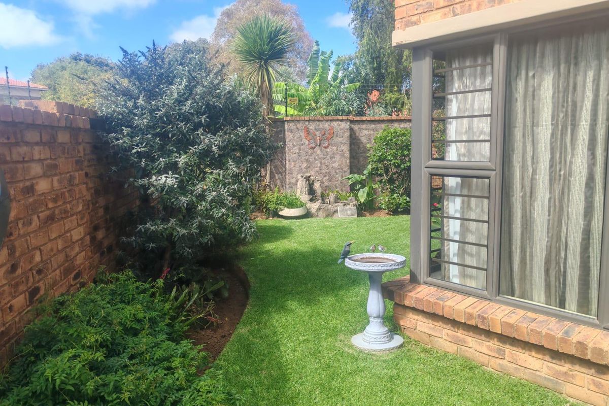 A private rear garden featuring a well-maintained lawn, established greenery, and face brick boundary walls, adjacent to the main dwelling with aluminium window frames.