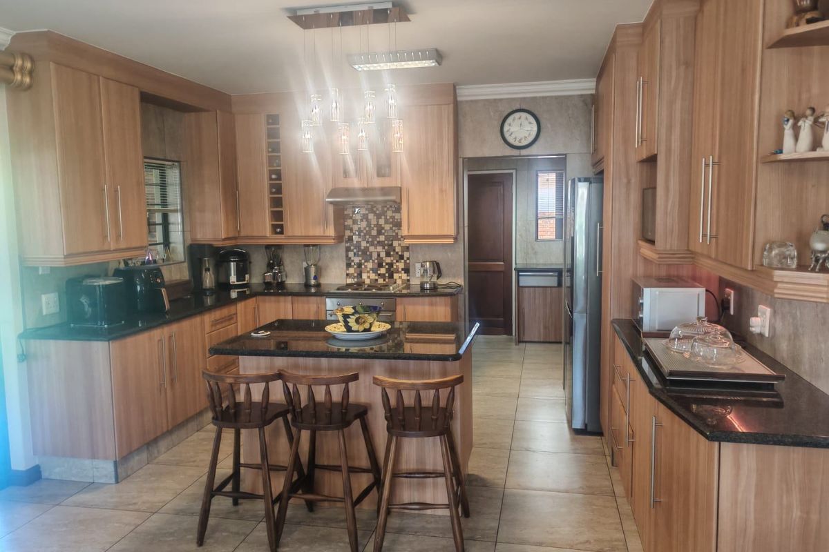 A well-maintained kitchen featuring wood-finish cabinetry, granite countertops, a central island with seating, and a mosaic tile backsplash.