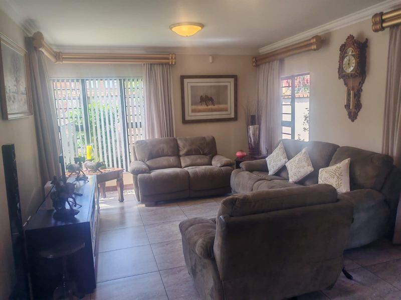 A comfortable living room featuring tiled flooring, decorative cornicing, and large windows with natural light.