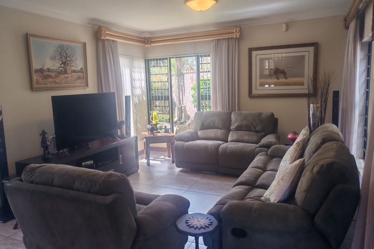A comfortable living room featuring tiled flooring, a corner window with security bars, and classic ceiling cornicing, providing a functional and well-lit space.