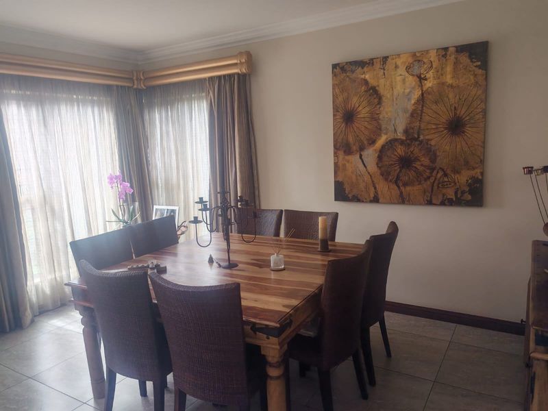 A well-maintained dining room featuring tiled flooring, decorative cornice, and large windows with curtain rails.