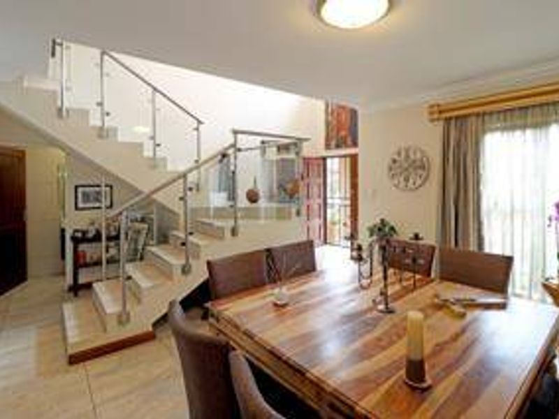 Open plan dining area featuring a modern staircase with glass balustrades and tiled flooring, leading to an exterior entrance.
