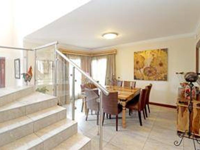 A bright dining area featuring tiled flooring, a coved ceiling, and a modern glass and stainless steel balustrade overlooking the staircase.
