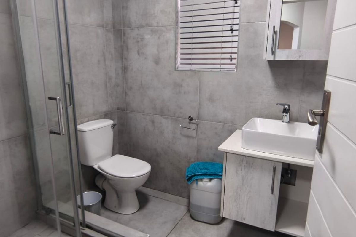 A modern bathroom featuring a glass shower enclosure, a vessel sink with a vanity cabinet, and neutral grey wall and floor tiling.