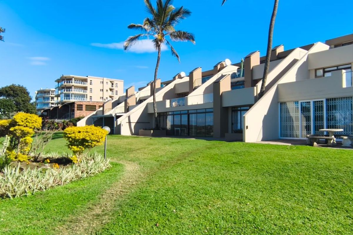 Rear view of the apartment complex featuring a well-maintained lawn, paved patio areas, and glass-fronted balconies with security gates.