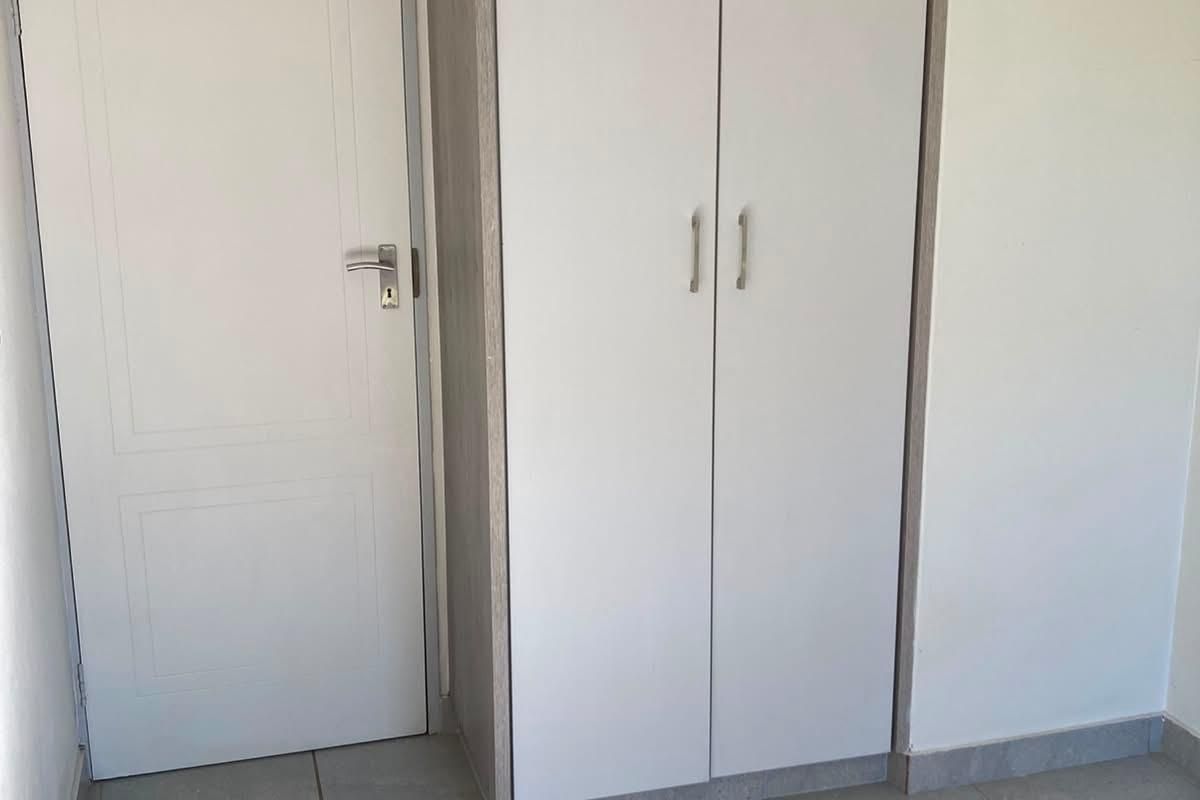 A clean, empty bedroom featuring neutral tiled flooring and a modern built-in cupboard with white doors.