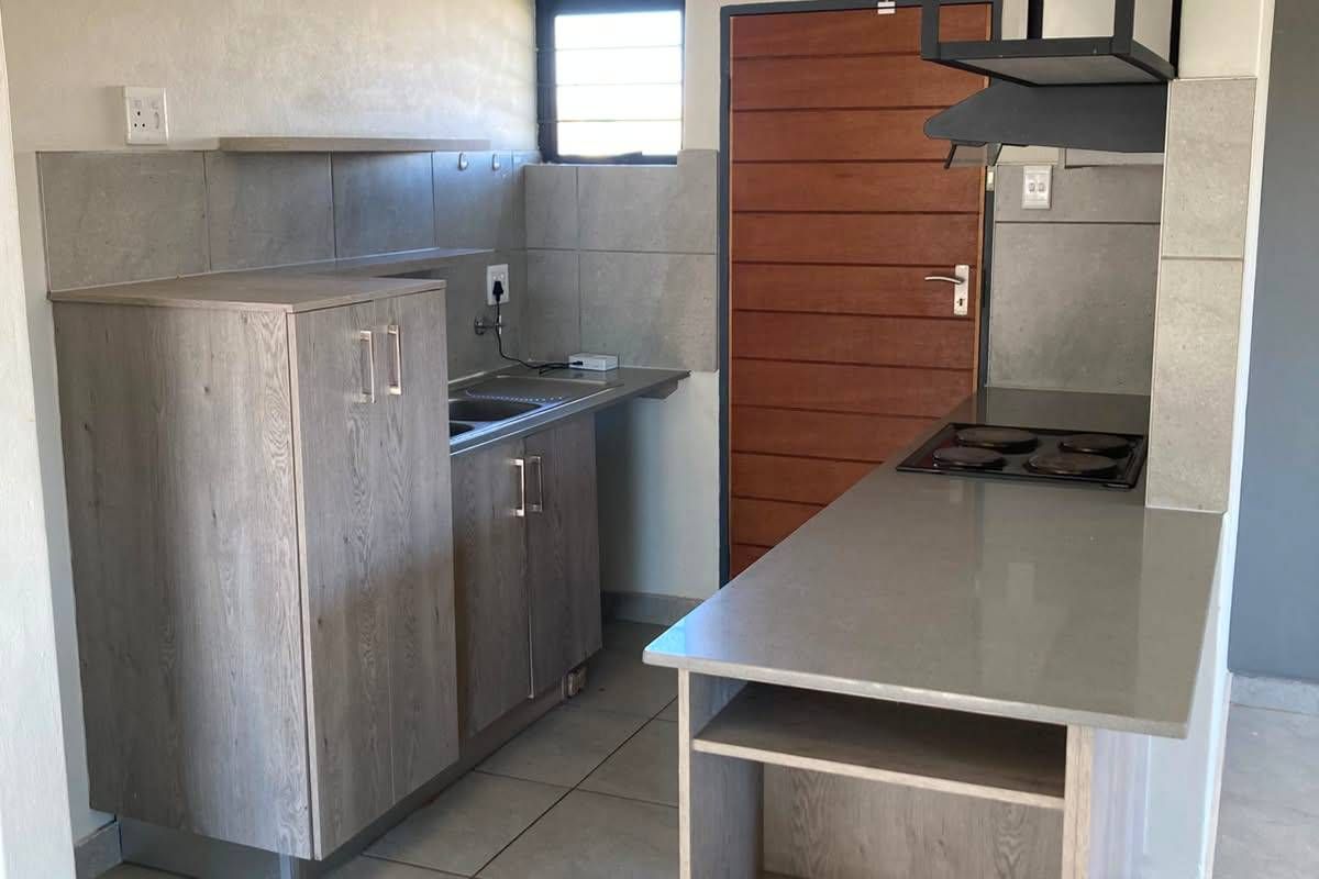 A modern, compact kitchen featuring grey wood-look cabinetry, stone countertops, an integrated electric hob, and neutral tiled flooring.