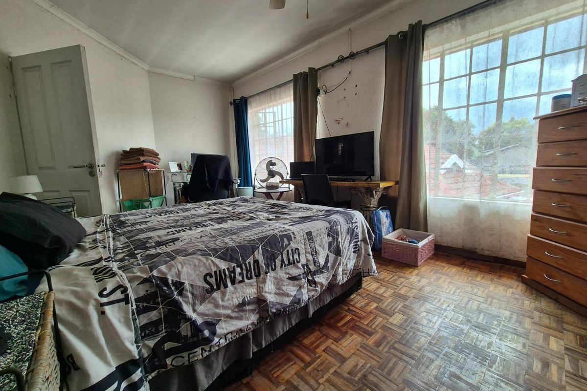 A bedroom featuring classic parquet flooring, a ceiling fan, and a large window providing natural light.