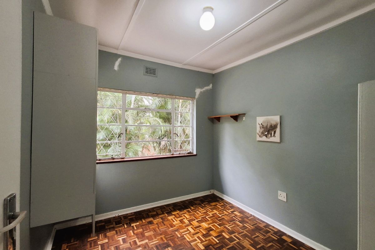 A vacant bedroom featuring original parquet flooring, a steel-framed window, and a built-in cupboard, requiring minor cosmetic repairs to the wall plaster.