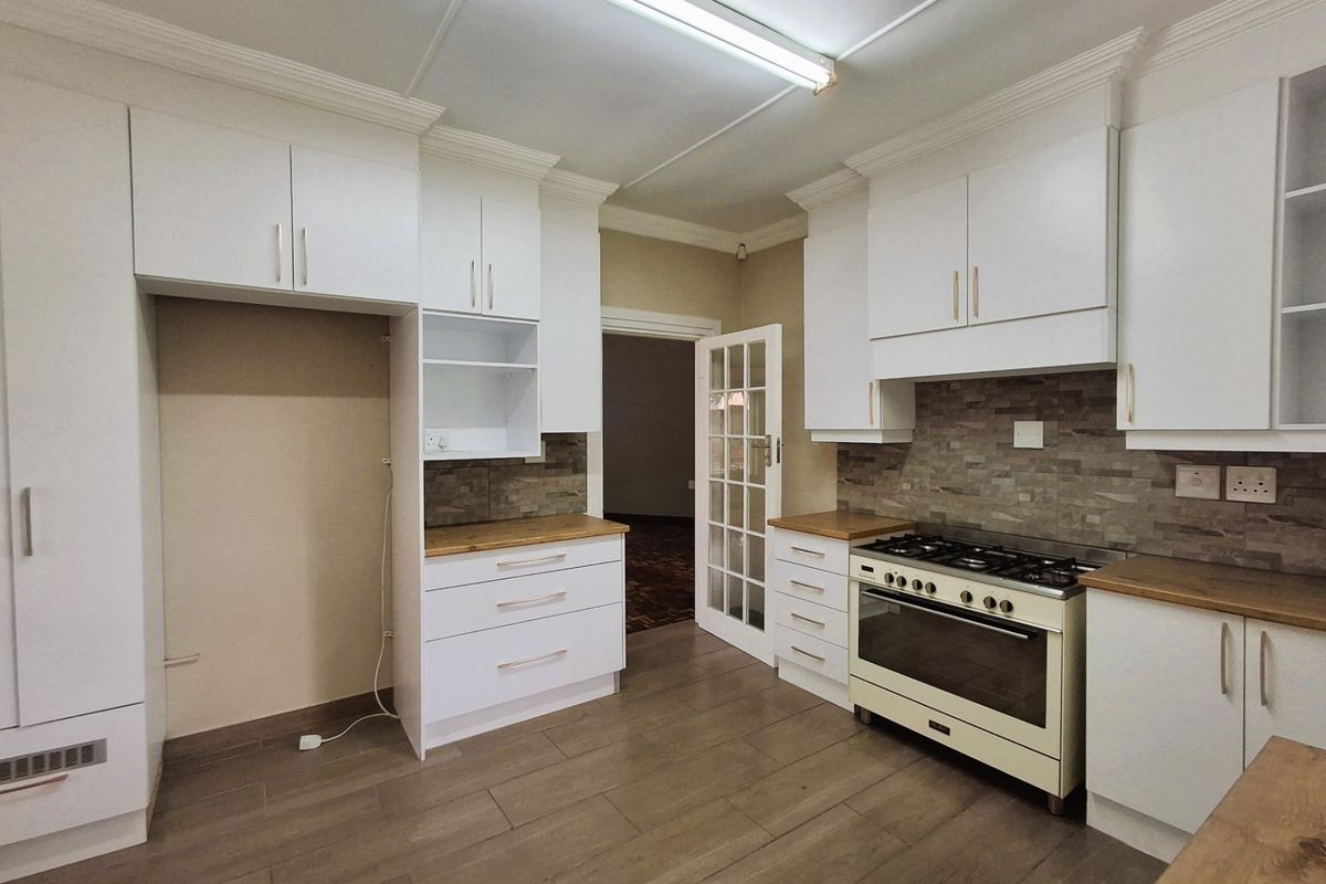 A clean, modern kitchen featuring white cabinetry, wooden countertops, a gas stove with oven, and stone tile backsplash, finished with neutral floor tiles.
