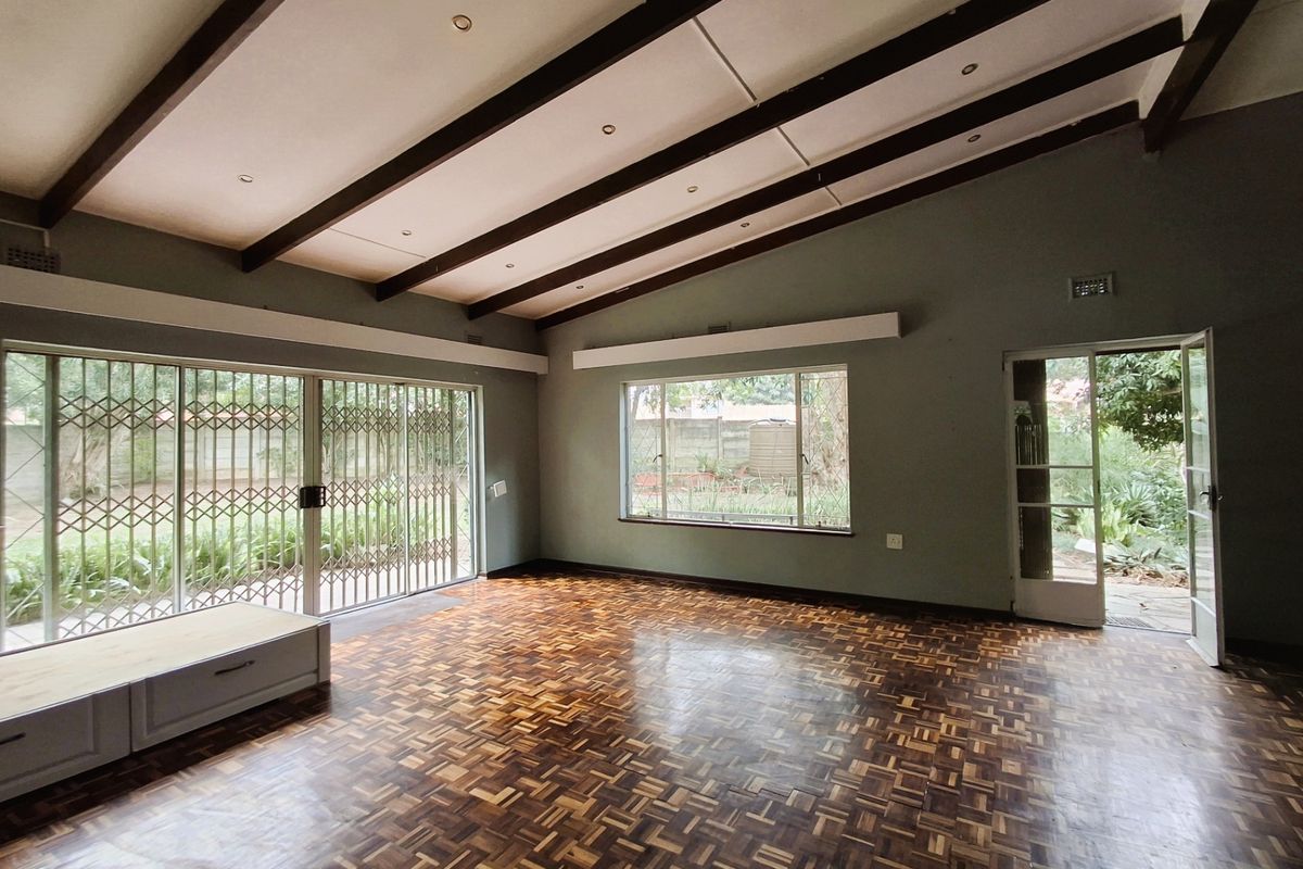 Spacious living room featuring classic parquet flooring, exposed timber ceiling beams, and large windows providing ample natural light and garden access.