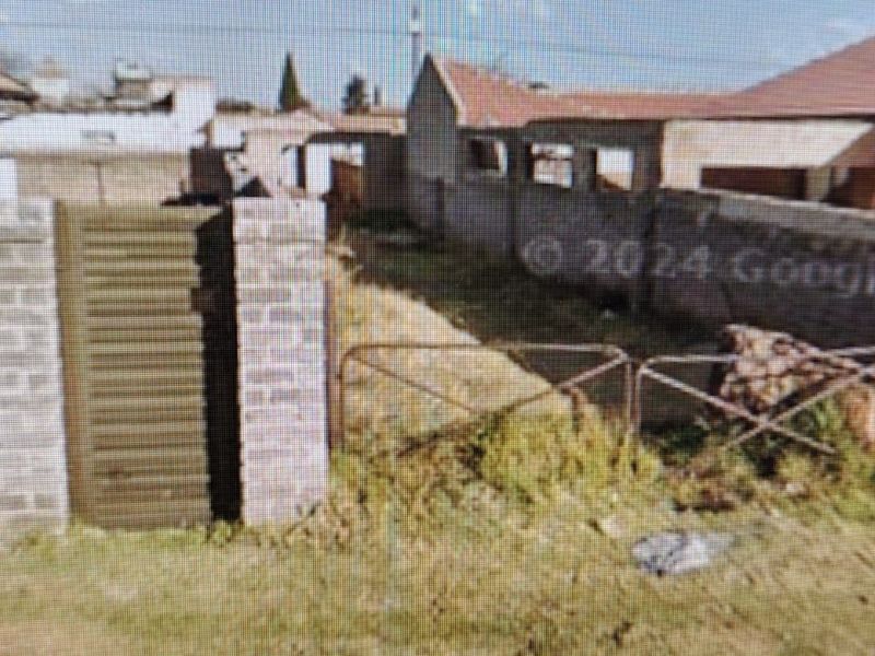 Rear exterior view of the property showing a brick boundary wall, metal gate, and unmaintained garden area.