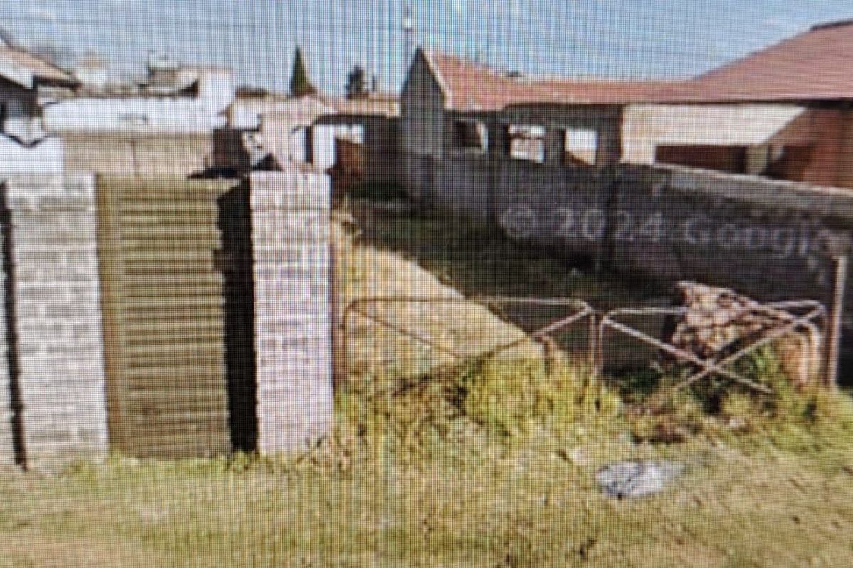 Rear exterior view of the property showing a brick boundary wall, metal gate, and unmaintained garden area.