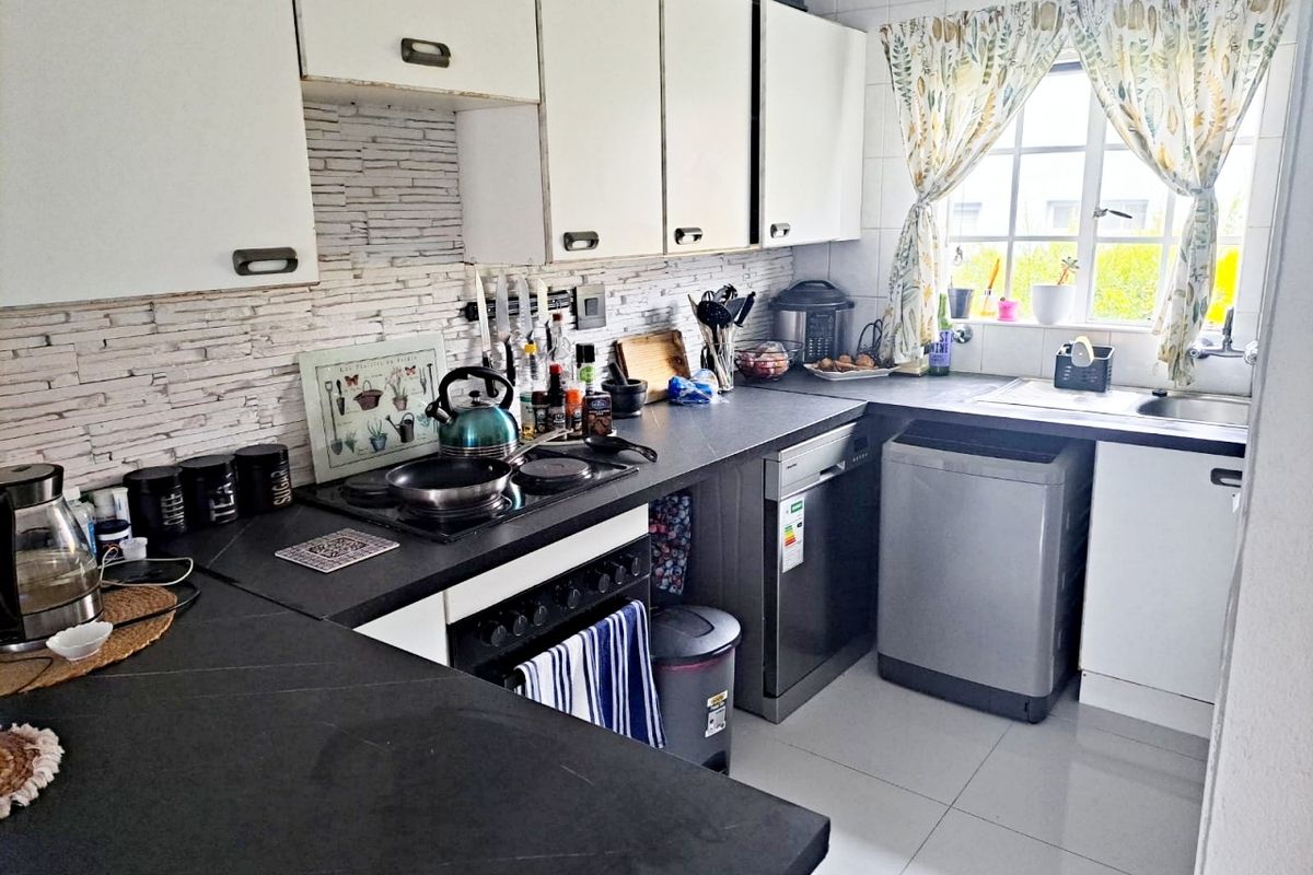 A functional kitchen featuring white cabinetry, dark laminate countertops, a built-in oven and hob, and a tiled backsplash with a window view.