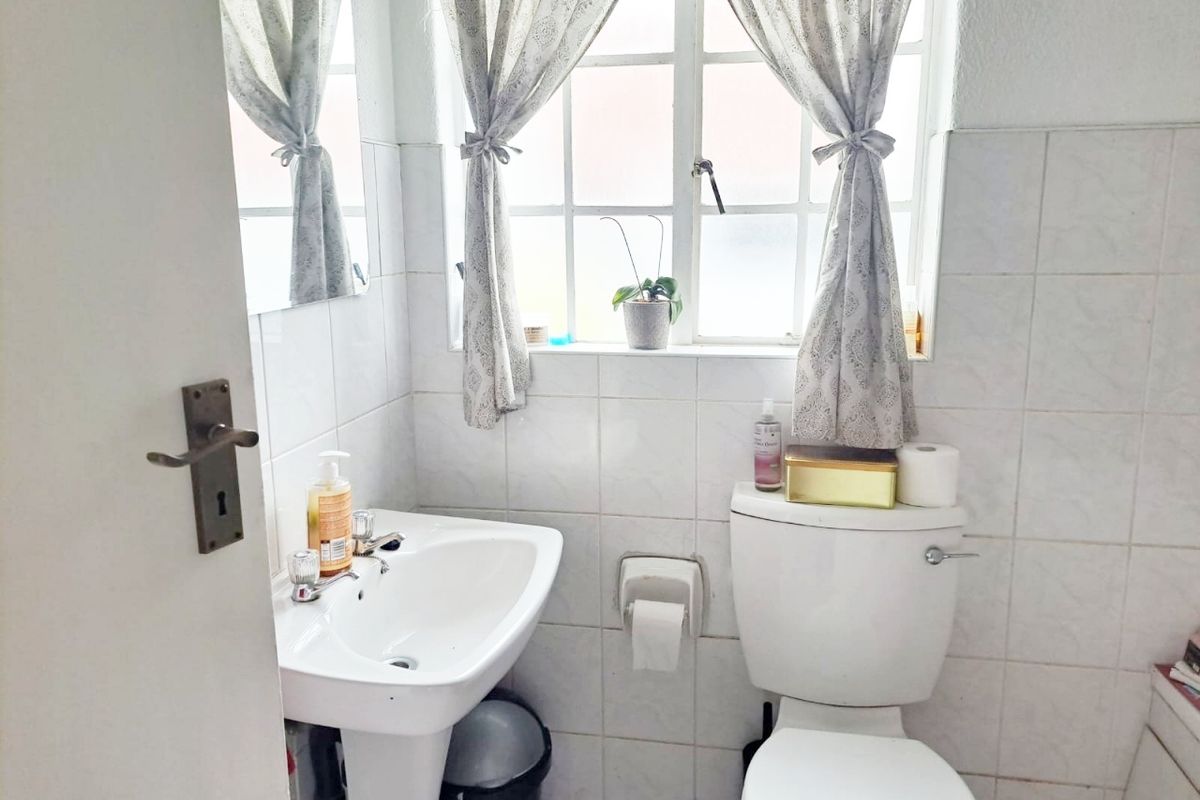 A functional bathroom featuring a pedestal basin, toilet, and tiled walls with natural light from a window.