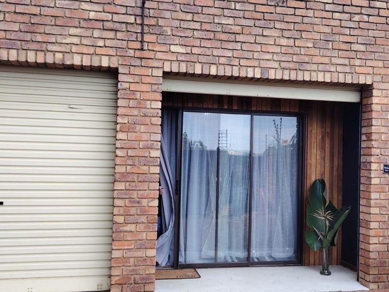 Front exterior view of a commercial property featuring a brick facade, a roller shutter garage door, and a sliding glass entrance door.