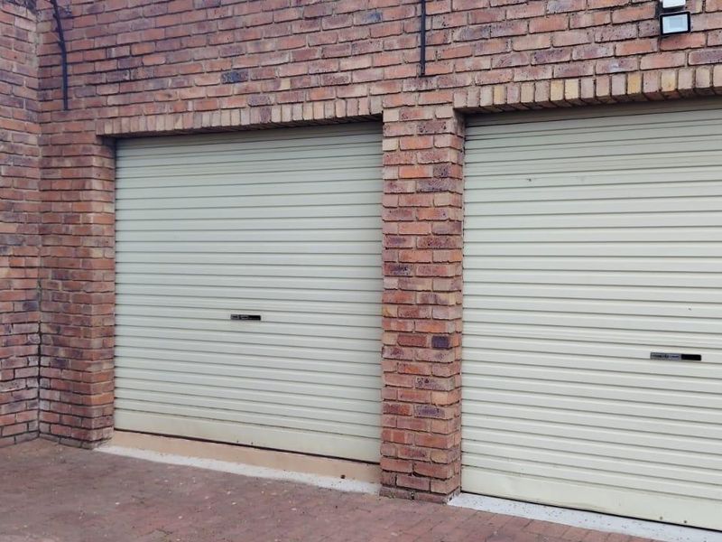 A double garage featuring brick exterior walls and two cream-colored roller doors with a paved driveway area.