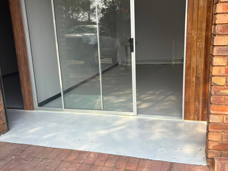 A paved patio area featuring a sliding glass door entrance with timber cladding and exposed brickwork detailing.