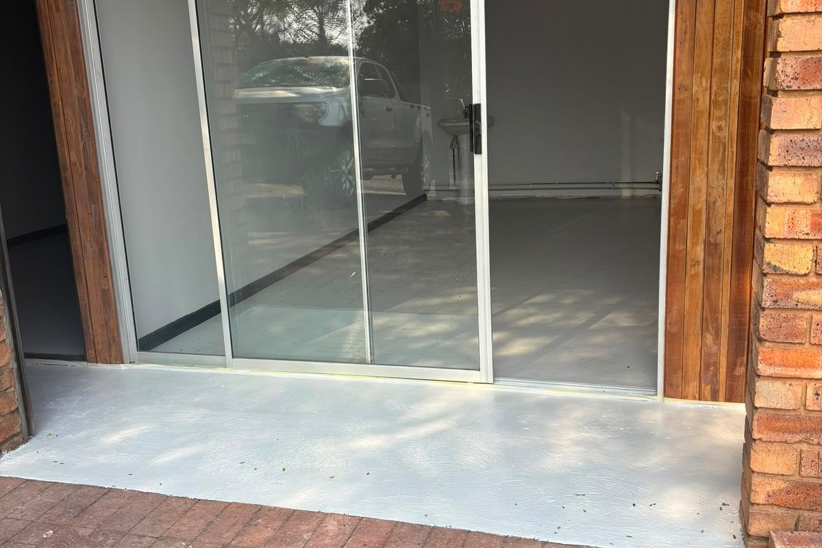 A paved patio area featuring a sliding glass door entrance with timber cladding and exposed brickwork detailing.