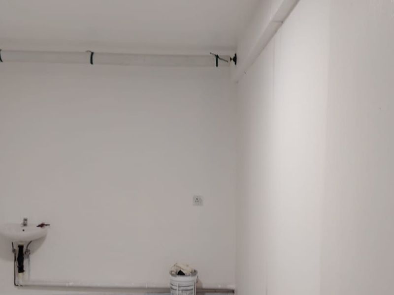 A functional utility space featuring a wall-mounted basin and exposed plumbing infrastructure, suitable for storage or service use.