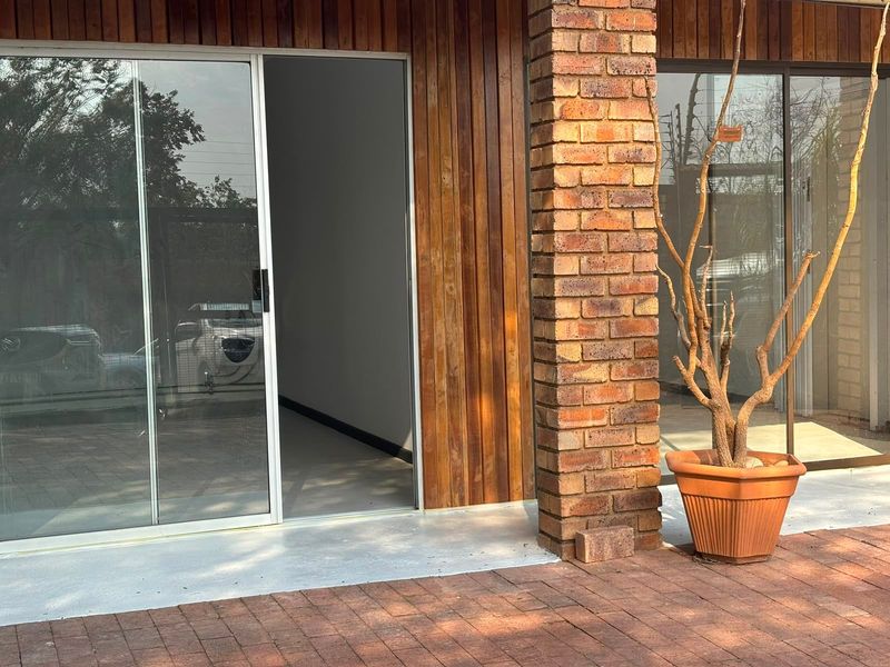 A modern commercial patio area featuring timber wall cladding, an exposed brick pillar, and large sliding glass doors leading into the interior space.