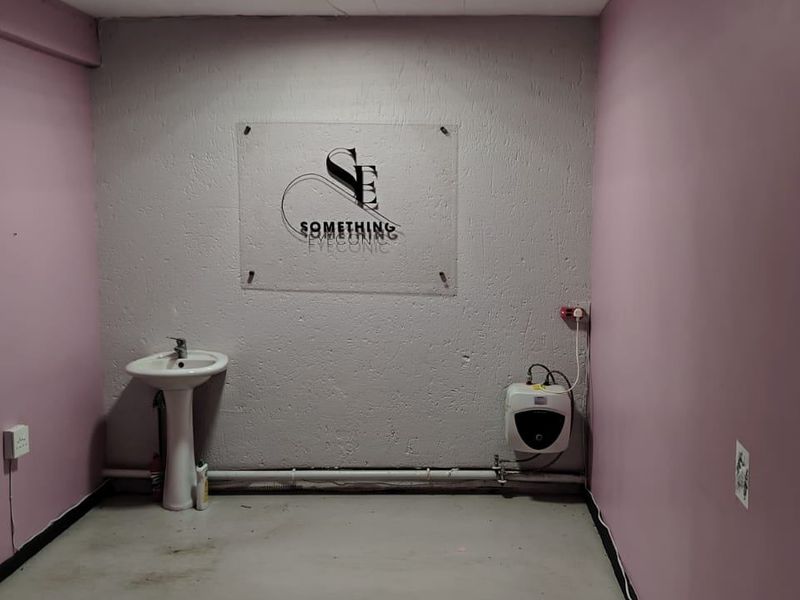 A functional utility space featuring a pedestal basin, an electric water heater, and exposed plumbing connections against a textured wall.