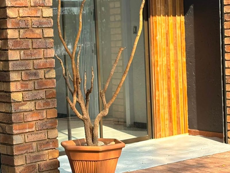 A covered patio area featuring brick paving, an exposed brick pillar, and timber slat wall cladding with a sliding glass door entrance.