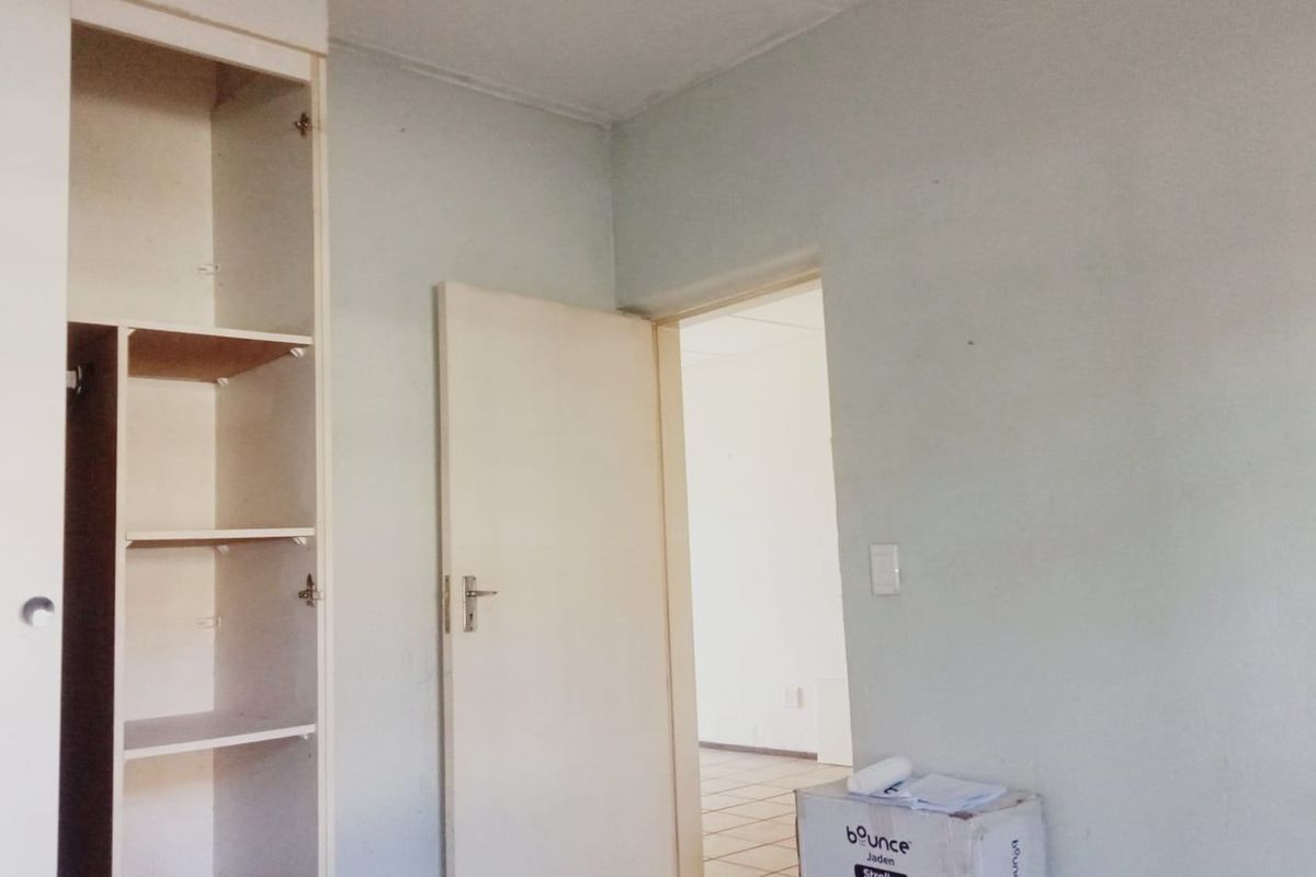 A vacant bedroom featuring a built-in wardrobe and a doorway leading to an adjacent room, requiring cosmetic updates to improve its overall condition.