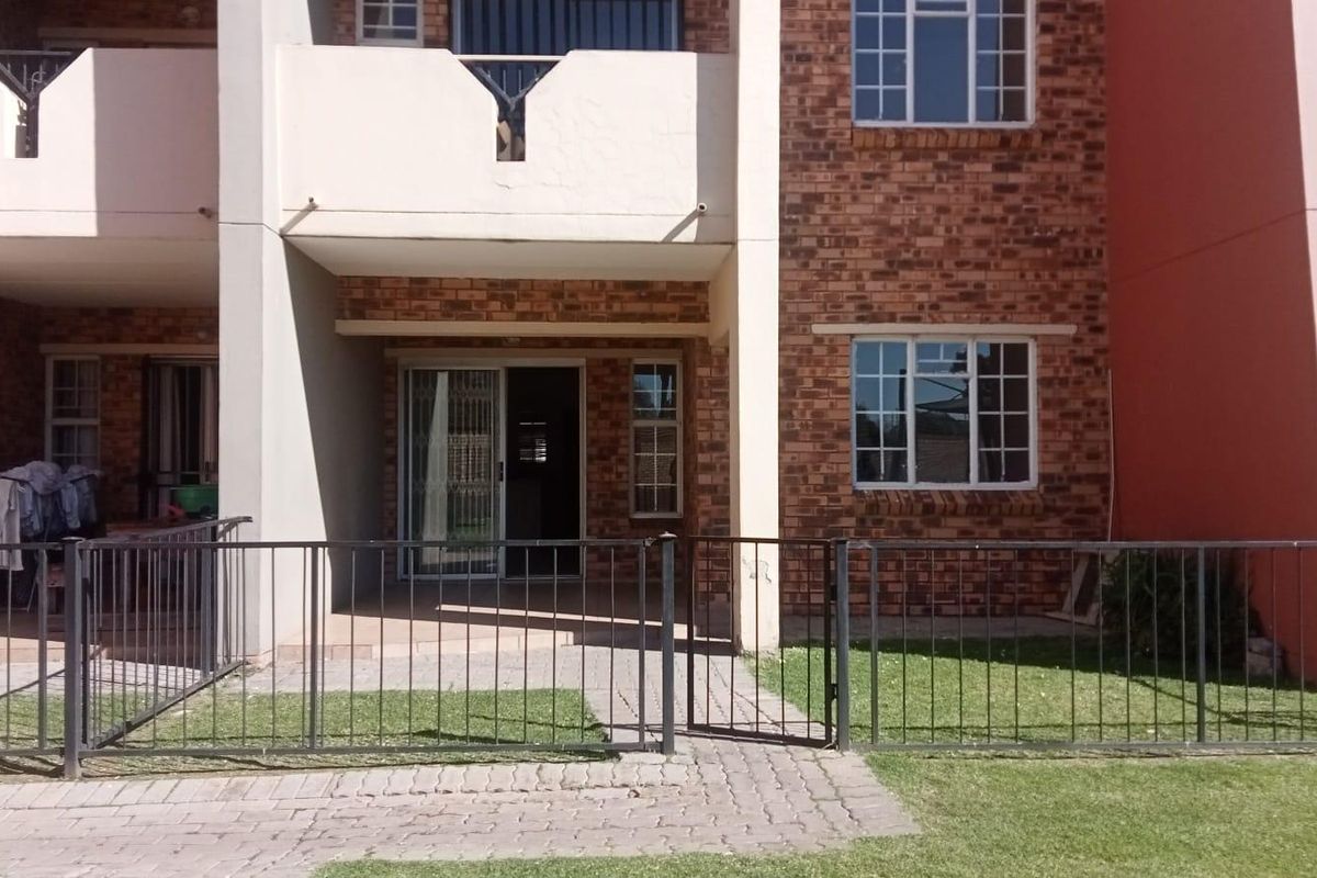 Rear view of an apartment unit featuring a brick facade, a ground-floor patio area with a sliding glass door, and a private fenced garden space.