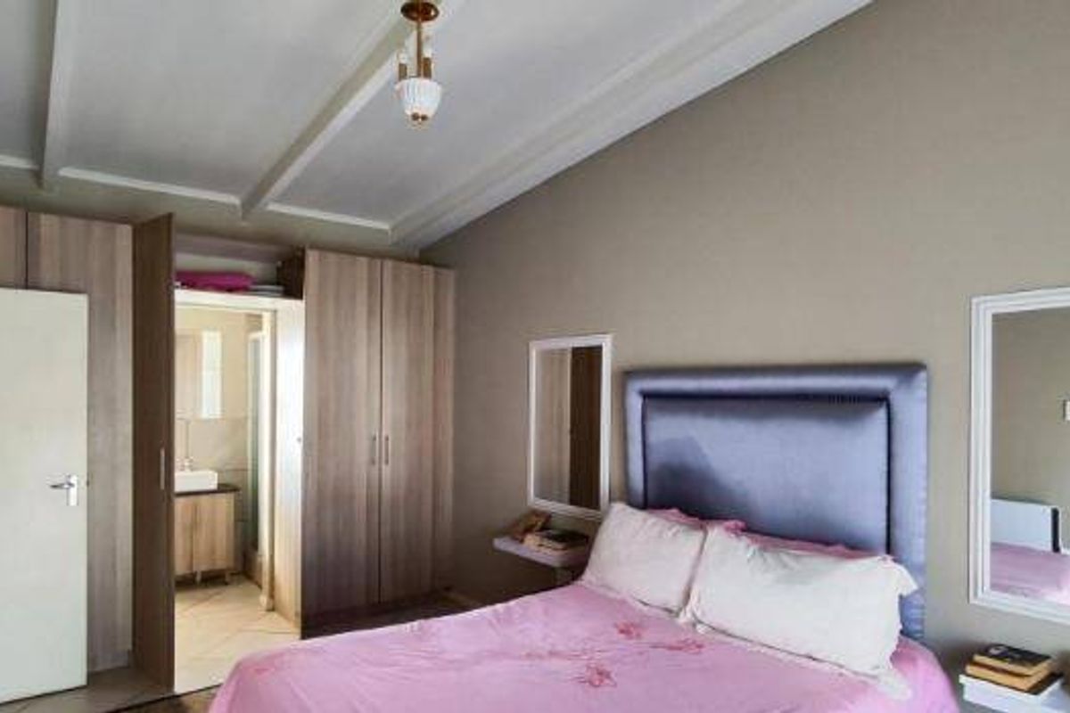 A well-maintained bedroom featuring built-in wooden cupboards, decorative ceiling beams, and direct access to an en-suite bathroom.