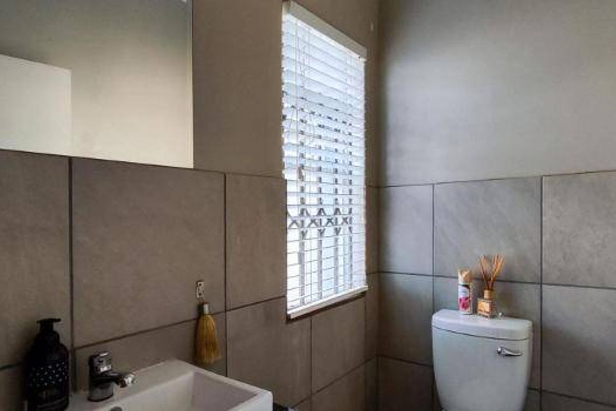 A functional bathroom featuring neutral ceramic wall tiles, a modern dual-flush toilet, a wall-mounted mirror, and a basin with chrome fixtures.