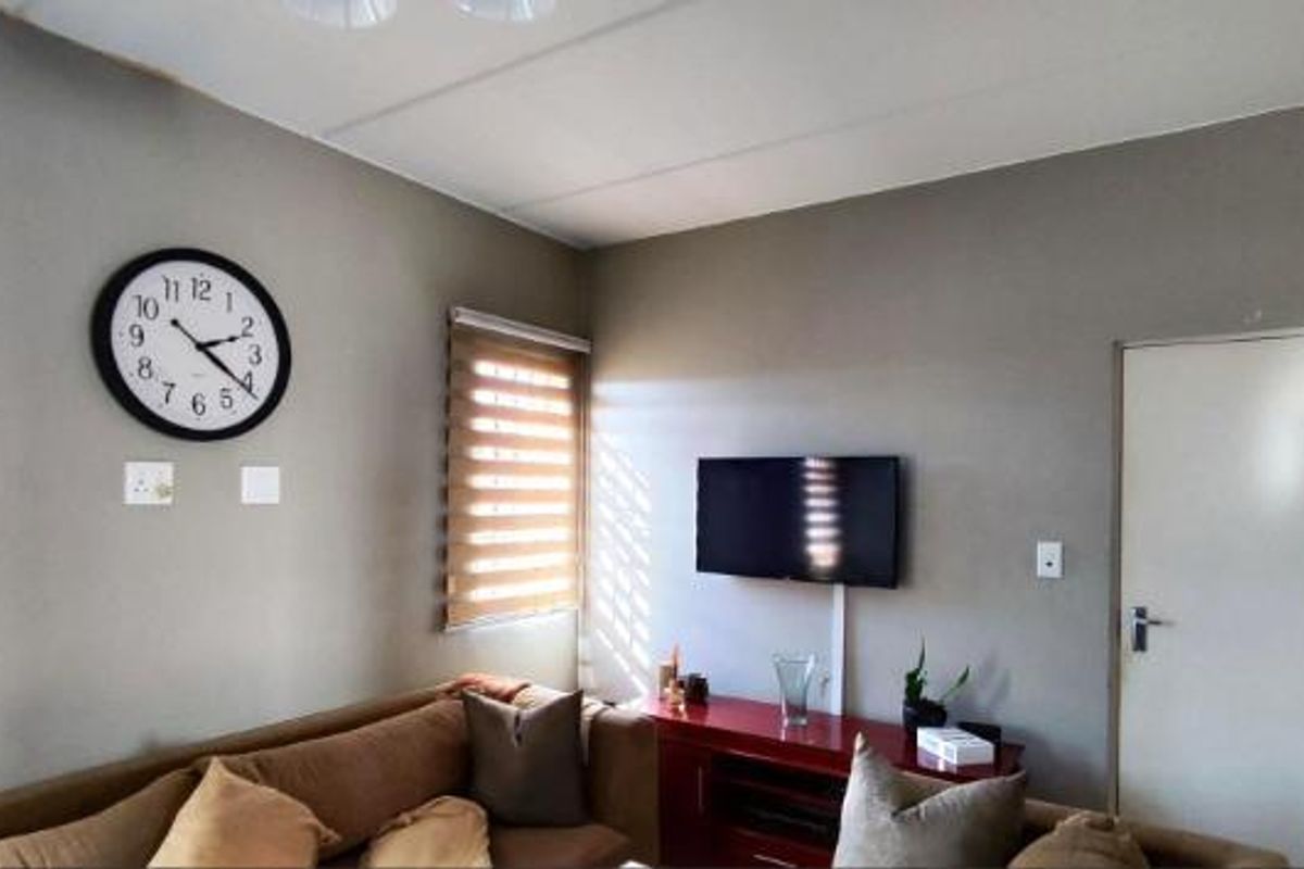 A functional living room featuring neutral wall tones, roller blinds, and wall-mounted television setup.