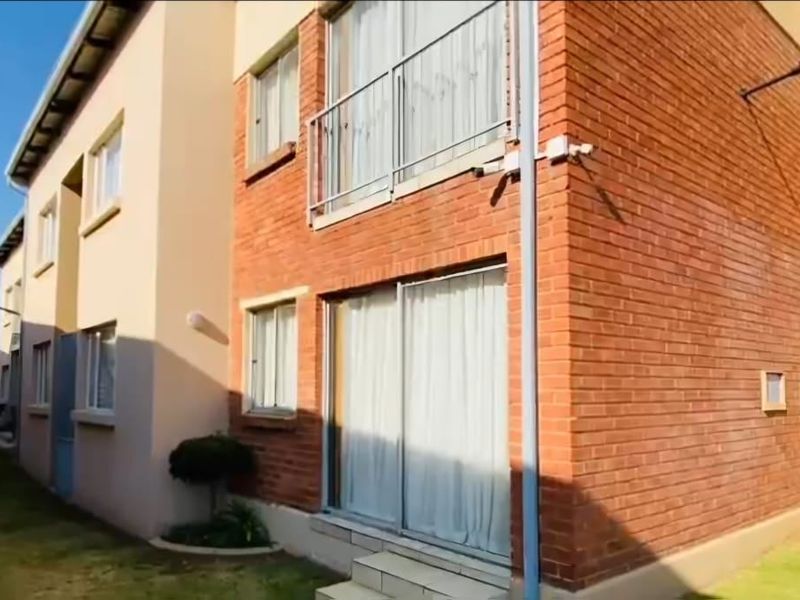 Rear exterior view of a multi-story commercial building featuring a brick facade, sliding glass doors, and an upper-level balcony with metal railings.