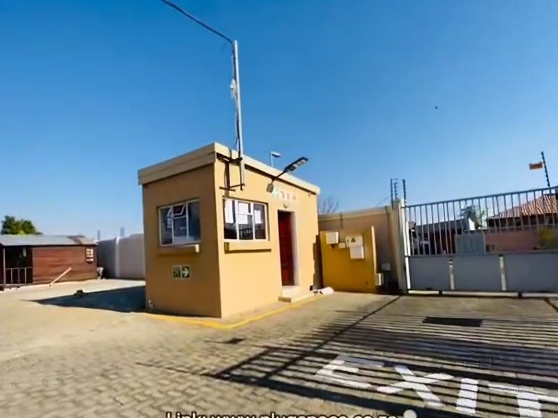 Commercial property entrance featuring a security guard house, paved driveway, and automated sliding gate with electric fencing for enhanced site security.