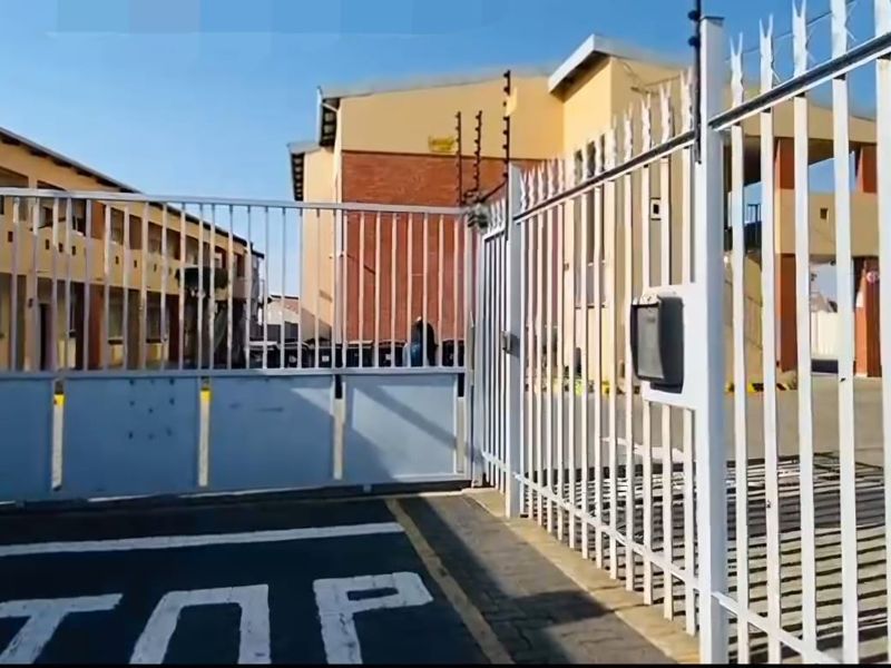 Front entrance view of a commercial property featuring a secure metal gate, electric fencing, and paved driveway access to the main building.